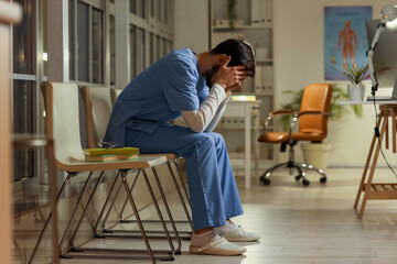 Tired male nurse sitting at hospital in evening