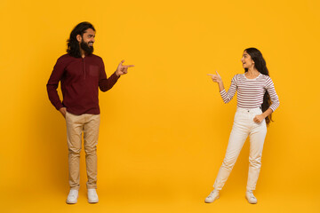 Man and woman pointing each other on yellow background