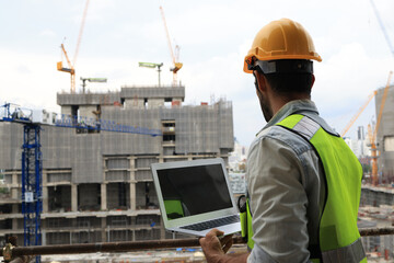 A project engineer at a construction site holds a laptop to track progress according to the plan....