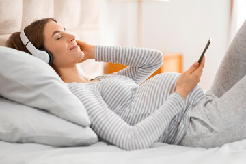 Woman lying on bed using smartphone and headphones