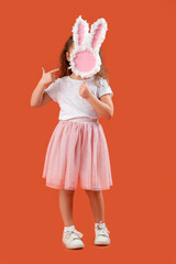 Cute little girl pointing at paper bunny figure on orange background. Easter celebration