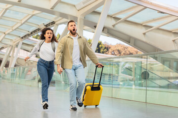 Couple running late in airport terminal - obrazy, fototapety, plakaty