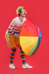 Portrait of clown with colorful umbrella on red background. April Fool's day celebration