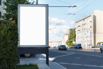Vertical blank white billboard on a city street. Bush, passing cars. Mock-up.