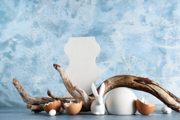 Decorative podiums with toy bunny, burning candles and tree branch on blue background