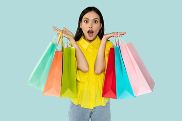 Fototapeta premium Excited surprised young woman with shopping bags at blue backgtound