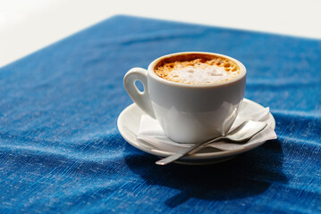 A white cappuccino cup on a blue tablecloth background