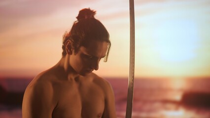 Person with sword posing at camera. Young man half naked with japanese sword katana poses in front digital screen with sunset skies.