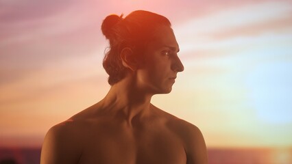 Profile of a young man with bare torso admiring a sunset, his face illuminated by the warm golden...