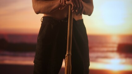 Person with sword posing at camera. Young man half naked with japanese kendo bamboo sword poses in front digital screen with sunset skies.