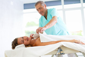 Obraz premium Relaxed middle-aged woman lying on massage table covered with soft blanket by kind masseuse