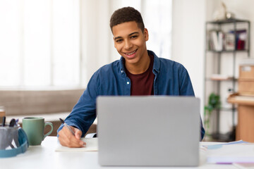 Smiling man writing notes with laptop