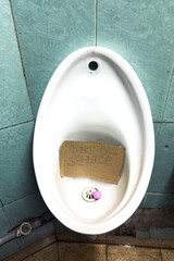 A dirty urinal basin in a washroom with an out of service sign indoors 
