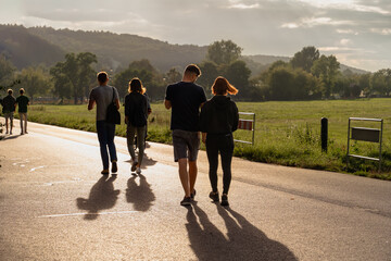 Couples leisurely stroll along a sun-drenched path, their silhouettes casting long shadows, evoking...