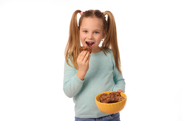 Smiling little girl holding and eating cookies or biscuits on white background