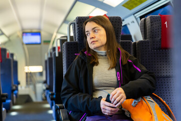 Relaxed dark-haired woman wearing black jacket traveling by modern train, sitting on comfortable...