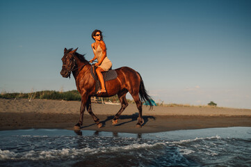A young woman is riding a horse on a seaside beach at summer.