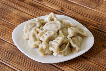 Cooked Russian dumplings with butter in a white plate on a wooden rustic table. National cuisine. Photo.