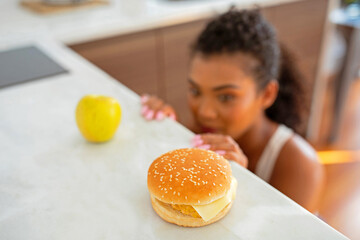 woman battles temptation at kitchen choosing between apple and cheeseburger