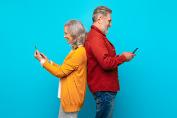 Elderly man and woman scrolling on their cell phones, studio