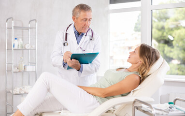 Fototapeta premium Male senior doctor conducts survey of female patient after procedure and fill in data in client medical record