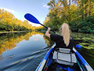 A young blonde woman is paddling in a kayak. Rear view. Tourism and outdoor recreation