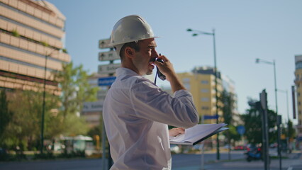 Hardhat architect talking instructions remotely at summer city street closeup