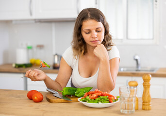 Obraz na płótnie Canvas Positive female eating healthy salad with fresh vegetable
