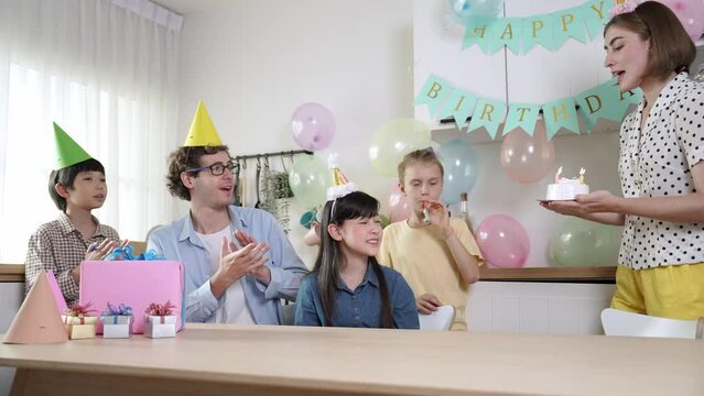 Happy girl celebrate her birthday while sing a song with lovely family while caucasian mother hold birthday cake. Attractive mom bring cake and walking in the room while wearing party hat. Pedagogy.