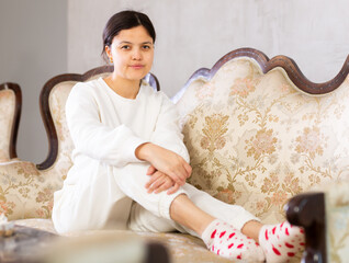 Calm pensive youthful brunette dressed casually in white clothing, sitting on comfortable...