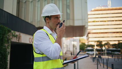 Building chief giving instructions workers using walkie-talkie in city closeup