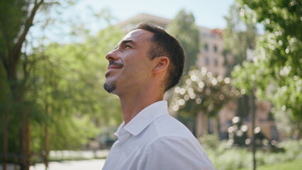 Smiling boss enjoying sunlight at summer city closeup. Brunette man at park
