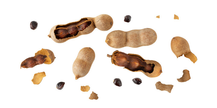 Ripe whole and sopen shelled tamarind fruits with seeds flying isolated on white background.