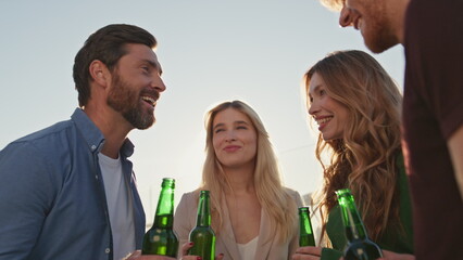 Joyful friends clinking beers relaxing together on rooftop party close up.