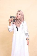 Fototapeta premium Beautiful Asian Muslim adult woman wearing a hijab with a cheerful expression tilted carrying prayer beads tied to the Koran while holding a dress. for advertising, lifestyle, banners and Ramadan