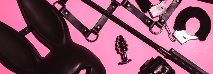 set of BDSM sex toys with handcuffs, whip flogger, butt anal plug for submission and domination on a pink background. Wide header cover for a horizontal banner for sex shop - obrazy, fototapety, plakaty