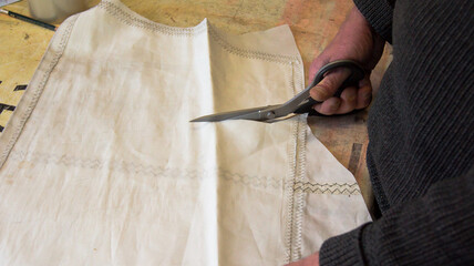 The tailor cuts out a piece of a white sail with a scissors to process it further.