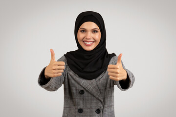 Joyful hijab-wearing woman giving thumbs up in suit