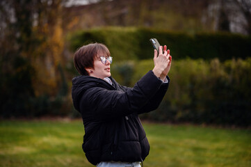 A delighted young woman takes a selfie, capturing the joy of a day spent in a verdant park, with her smartphone held high to get the perfect shot