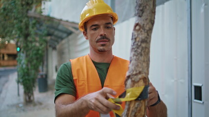 Guy putting warning tape at tree closeup. Builder man enclosing with stretch