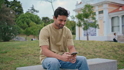 Obraz premium Smiling hipster messaging cellphone at urban bench close up. Happy guy texting
