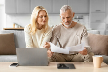Focused couple looking at documents by a laptop