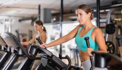Active athlete young woman engaged in intensive high interval training on ellipsoid simulator....