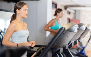 Girl walk on treadmill in gym. Active hobby, healthy lifestyle, extensive training. Happy sporty people interacting in weight room training - social gathering concept in sport lifestyle context