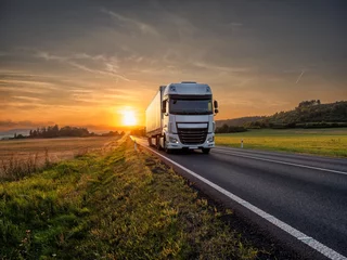 Fotobehang White truck driving on the asphalt road in rural landscape at sunset © am