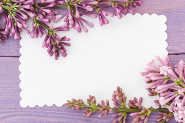Lilac branch and empty white card on lilac wooden surface