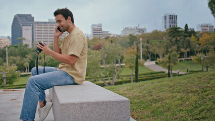 Fototapeta na wymiar Latin photographer talking smartphone in green park. Happy carefree guy calling 
