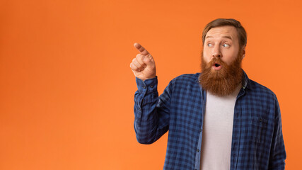 Fototapeta premium Amazed Redhaired Man Pointing Finger Aside At Empty Space, Studio