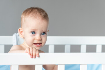 Baby with a vaguely distorted facial expression in a white classic crib
