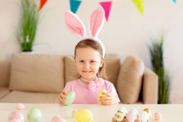 Cute girl wearing bunny ears on Easter day play with Easter eggs at the table at home